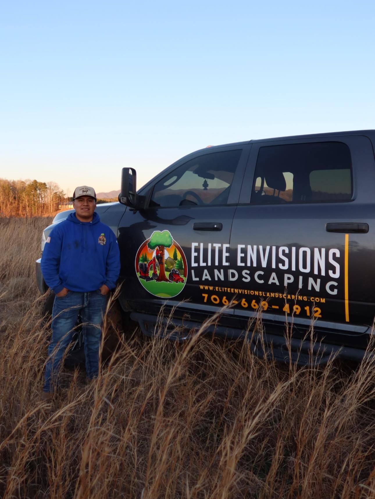 Woman in straw hat smiles, holding wine glass near a lake.