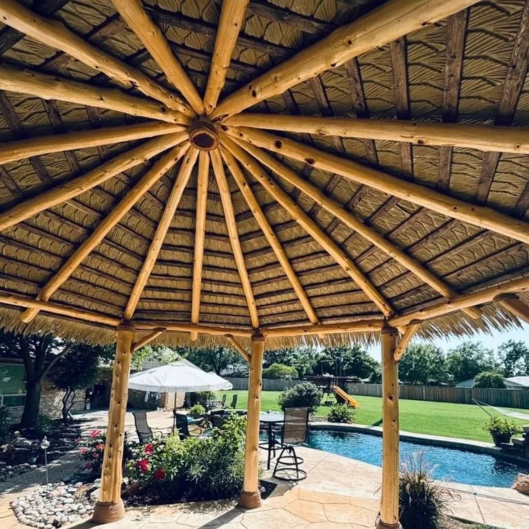 Gazebo with thatched roof, wooden beams, overlooking a pool and backyard.