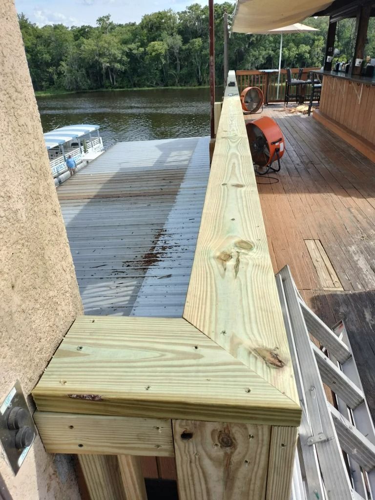 Wooden deck with a handrail, next to a dock on a river.