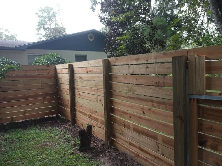 Wooden fence in a backyard, brown wood, with a house in the background and green grass.
