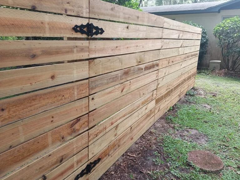 Wooden horizontal slat fence in a yard, with a decorative black hinge.