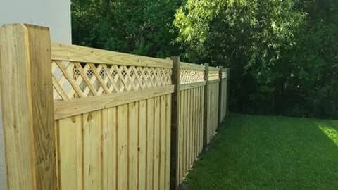 Wooden fence with lattice top in a yard with green grass and trees.