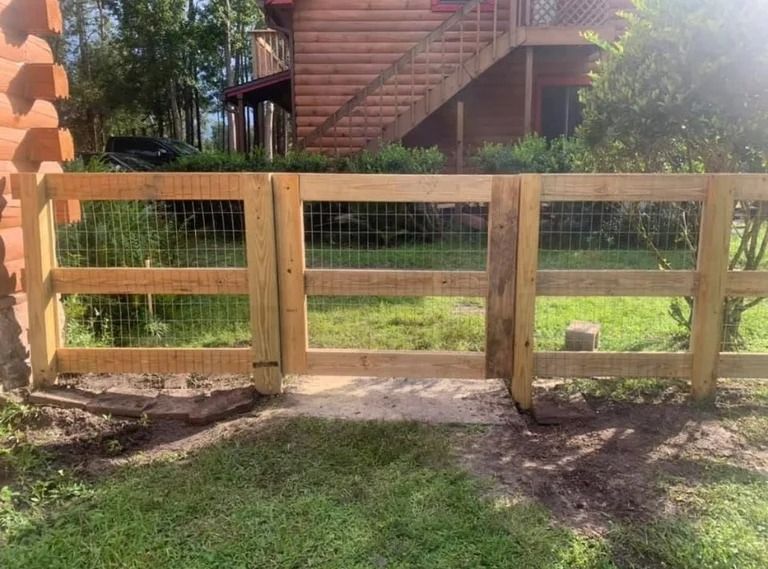 Wooden fence with wire mesh in front of a log cabin with a gate.