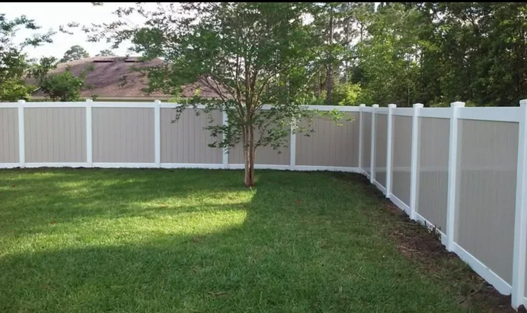 Green grass yard with a light-colored vinyl fence and a small tree in the center.