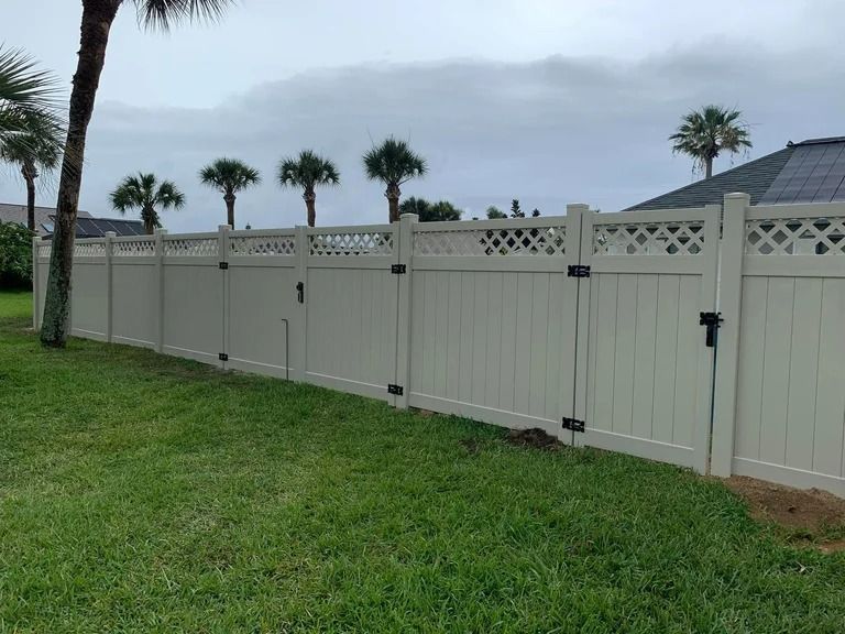 White vinyl fence with lattice top, enclosing a grassy yard with palm trees in the background.