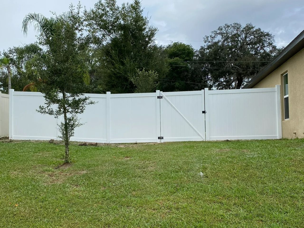 White vinyl fence in a backyard with a gate, green grass, and trees.