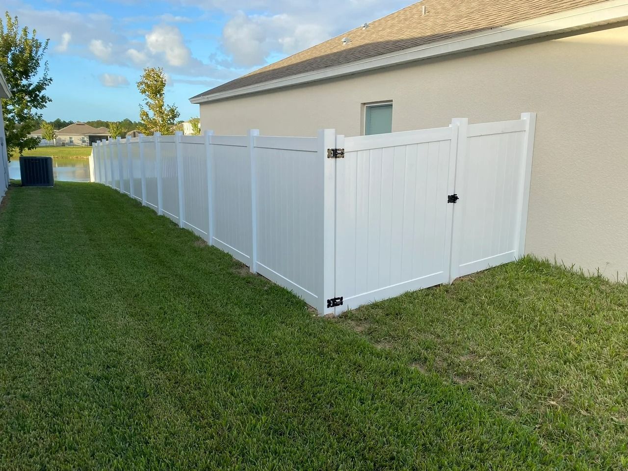White vinyl fence enclosing a green lawn next to a beige house under a blue sky.