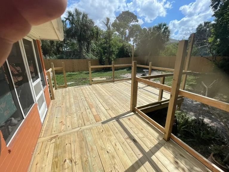 Wooden deck with railings, built next to an orange house, overlooking a yard with a wooden fence.