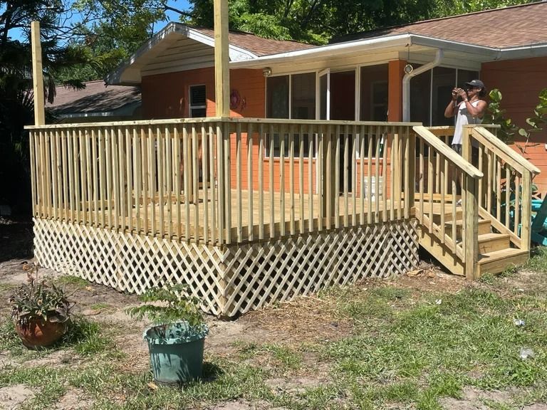 Wooden deck with lattice skirting, railings, and steps, attached to a house with an orange exterior.