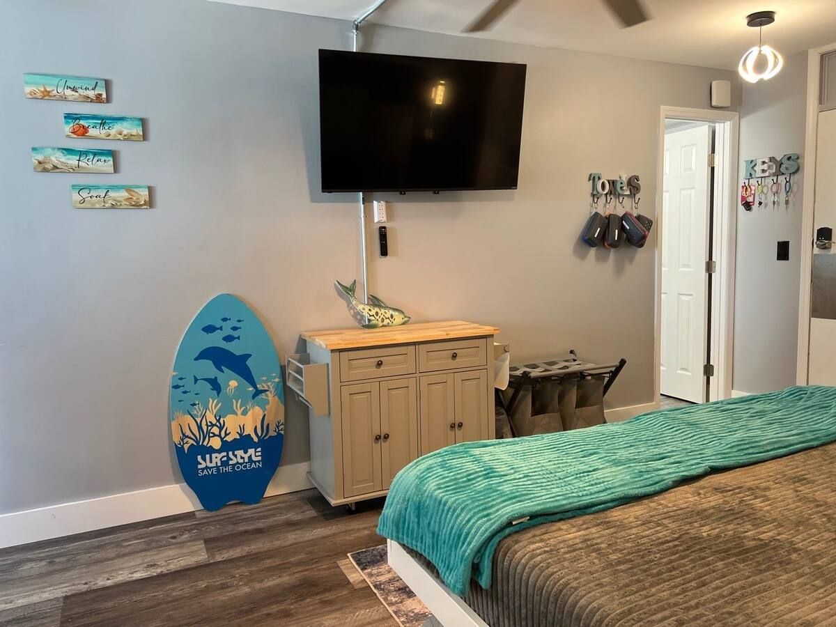 A bedroom with a bed , dresser , television and surfboard.