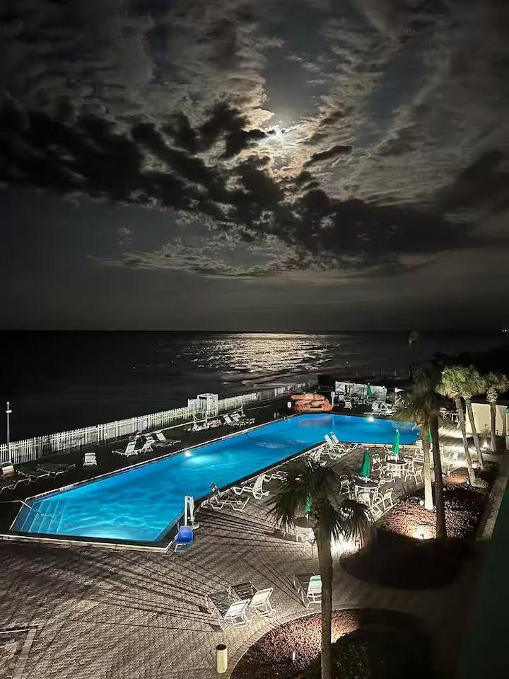 A large swimming pool is lit up at night with a full moon in the sky.