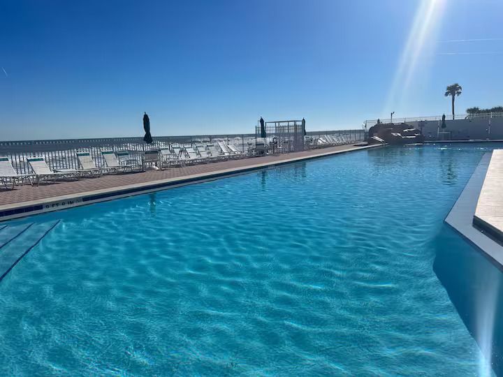 A large swimming pool with a view of the ocean on a sunny day.