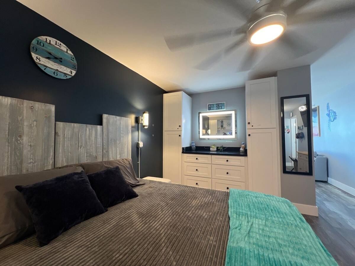 A bedroom with a king size bed , a ceiling fan and a mirror.