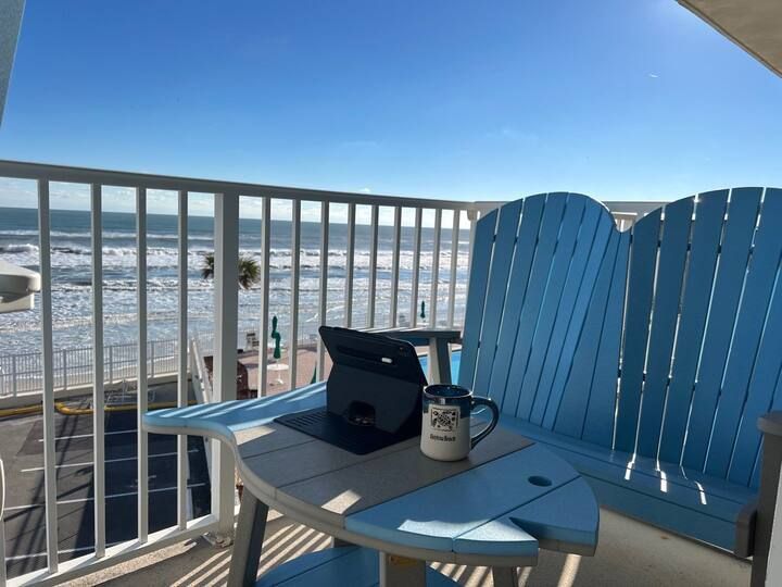 A tablet sits on a table on a balcony overlooking the ocean