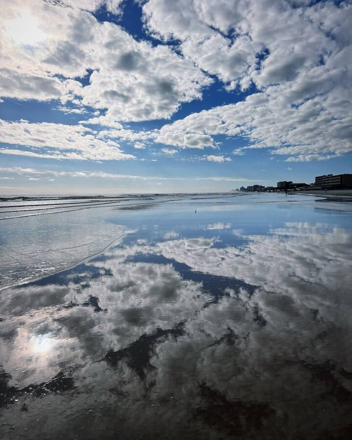 A beach with a blue sky and clouds reflected in the water