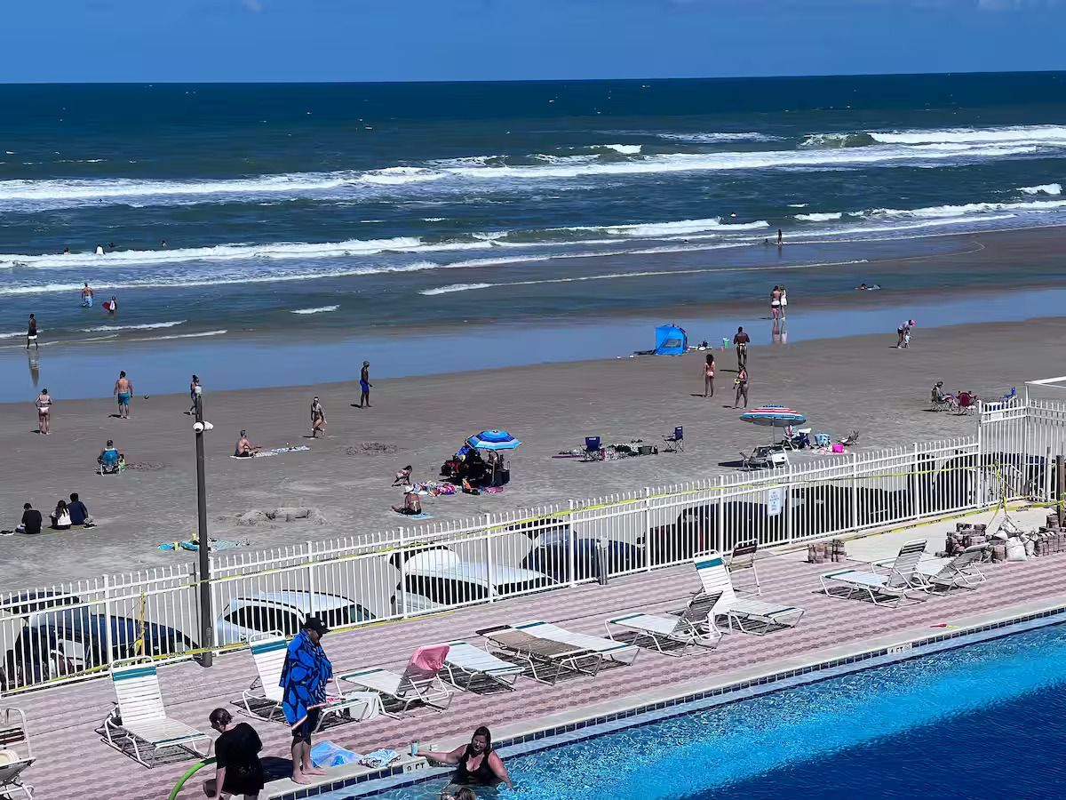 A swimming pool surrounded by chairs and umbrellas next to a beach.