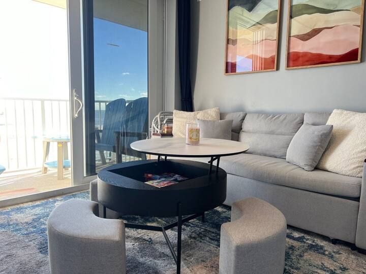 A living room with a couch , table , ottomans and a balcony.