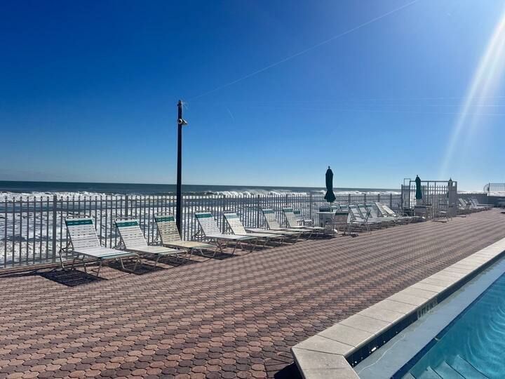 A swimming pool with chairs and umbrellas next to the ocean.