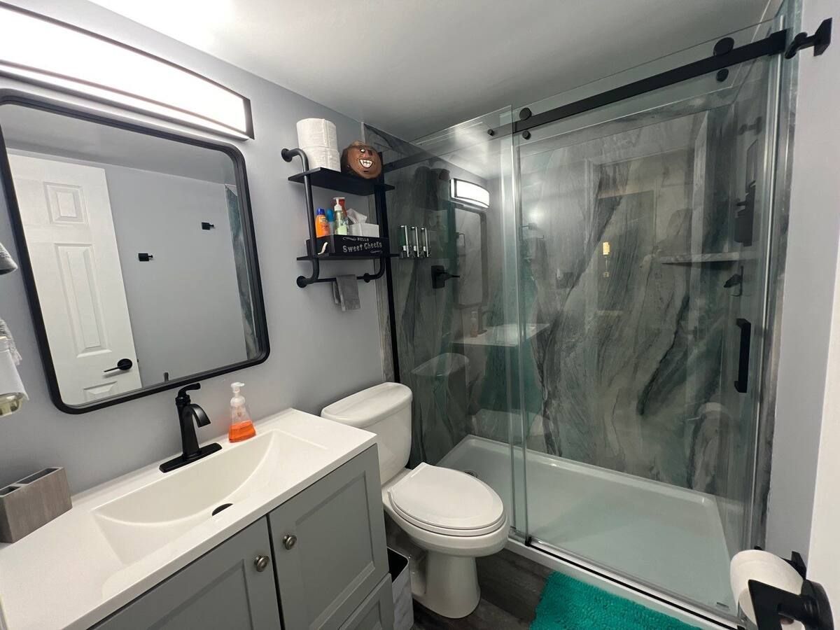 A bathroom with a toilet , sink , mirror and shower.