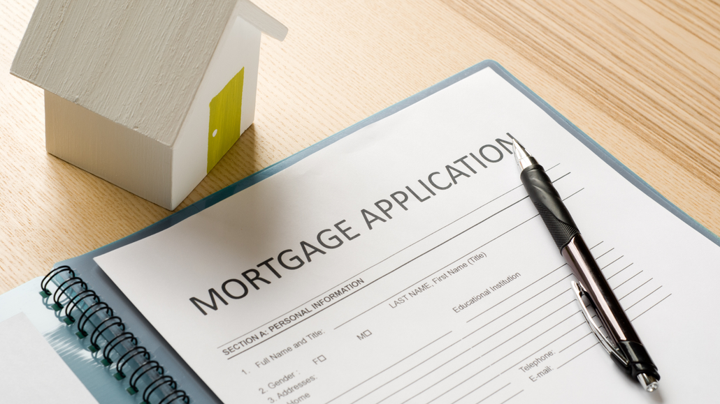 A mortgage application with a pen and a model house on a wooden table.