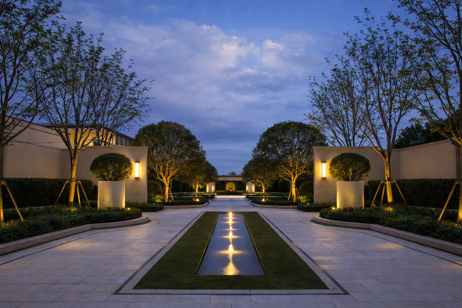 A symmetrical outdoor walkway with illuminated trees and a central water feature, under a dusky blue sky.