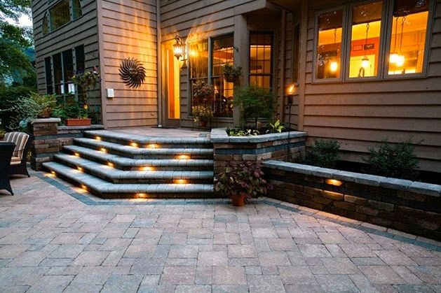 Lit steps leading to a house at dusk. Exterior features include stone walls, landscaping, and warm lighting.