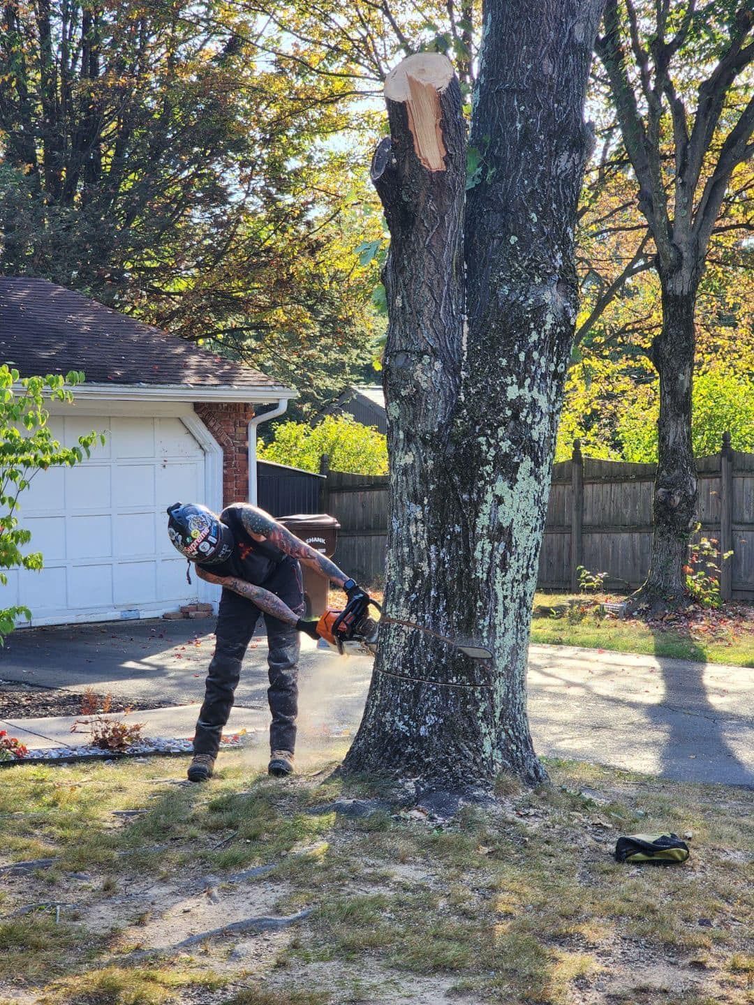 A man is cutting a tree with a chainsaw in front of a garage.