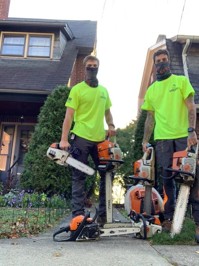 Two men standing next to each other holding chainsaws in front of a house.