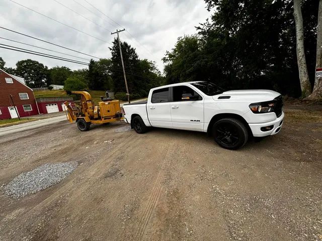 A white truck is towing a yellow machine down a dirt road.