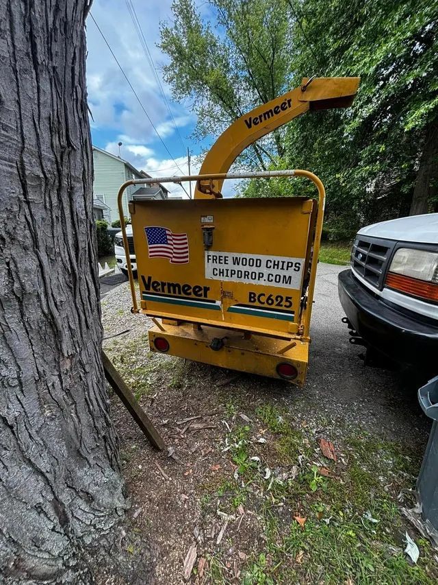A yellow tree chipper is parked next to a tree.