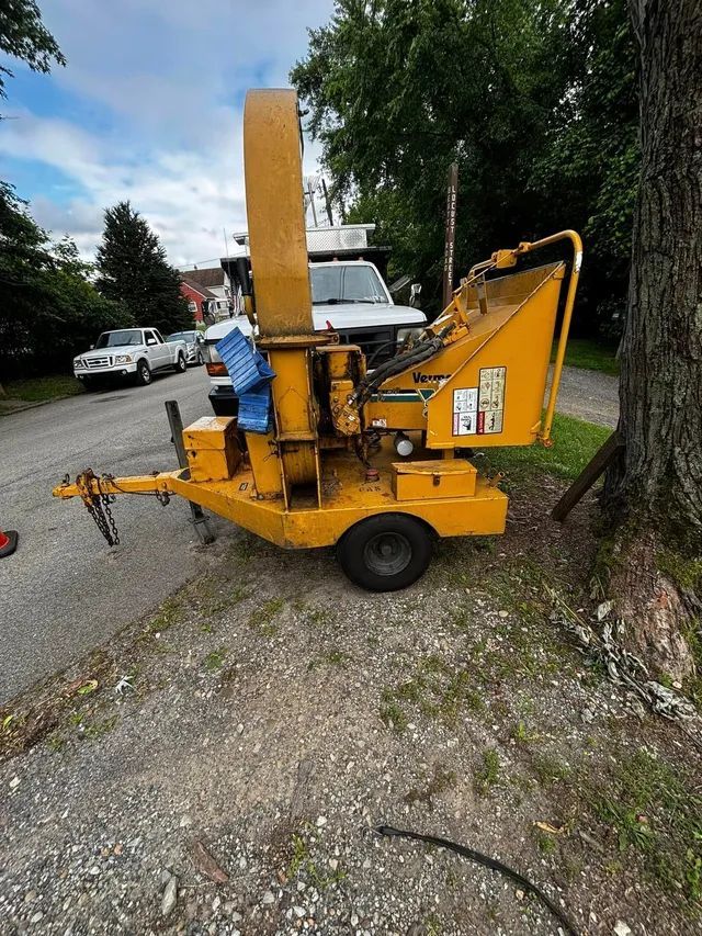 A yellow tree chipper is parked on the side of the road next to a tree.