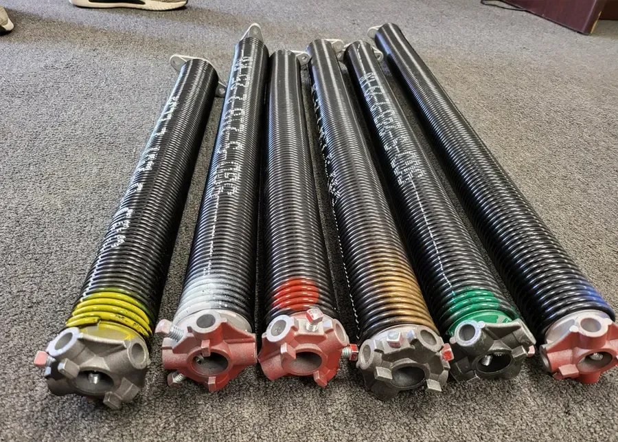 Six garage door torsion springs with different colored ends on a carpet.