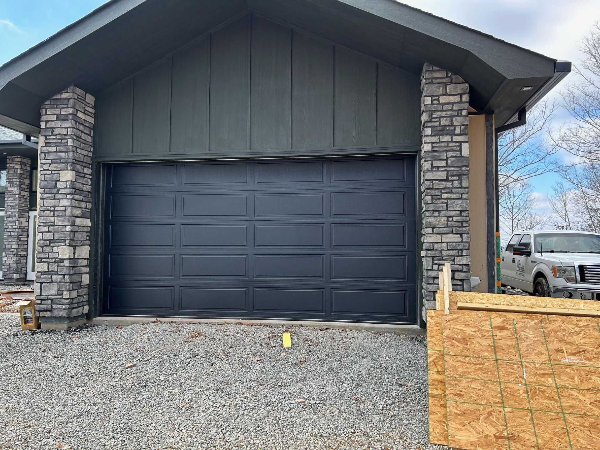 Dark gray garage door with stone pillars. A white truck is parked nearby. Dark gray garage door with stone pillars. A white truck is parked nearby.