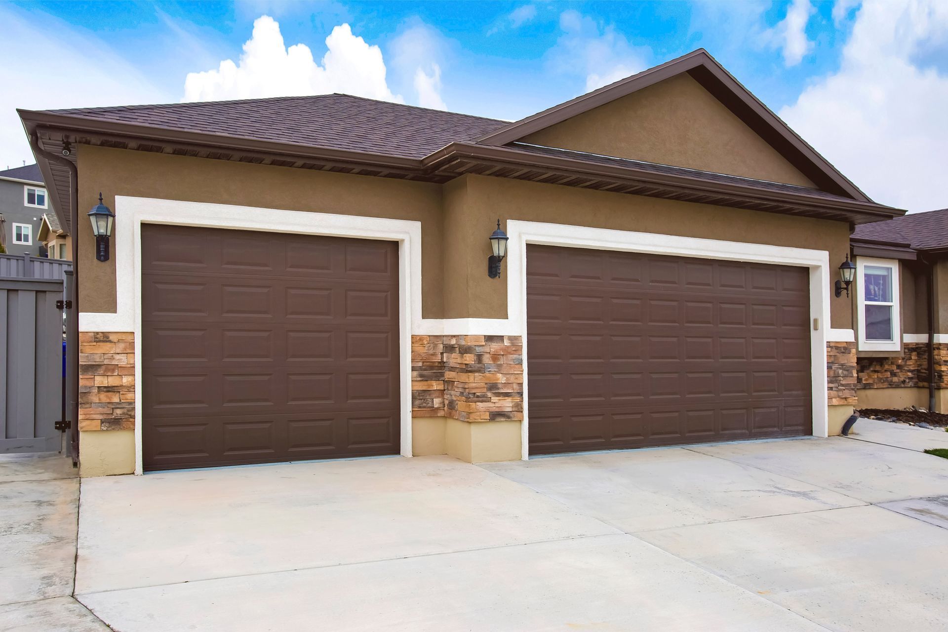 Two-car garage with brown doors, beige trim, and stone accents, under a brown roof, against a blue sky.