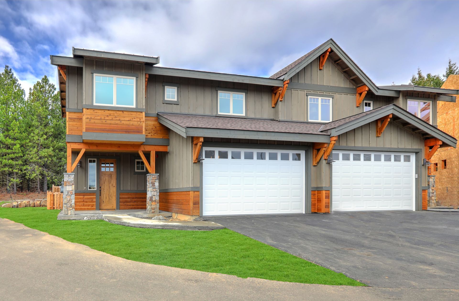Two-story home with gray siding, wood accents, and two-car garage. Green lawn and driveway in front.