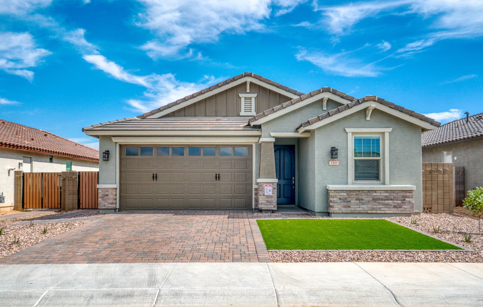 A single-story house with a brown garage door, green lawn, and blue sky.