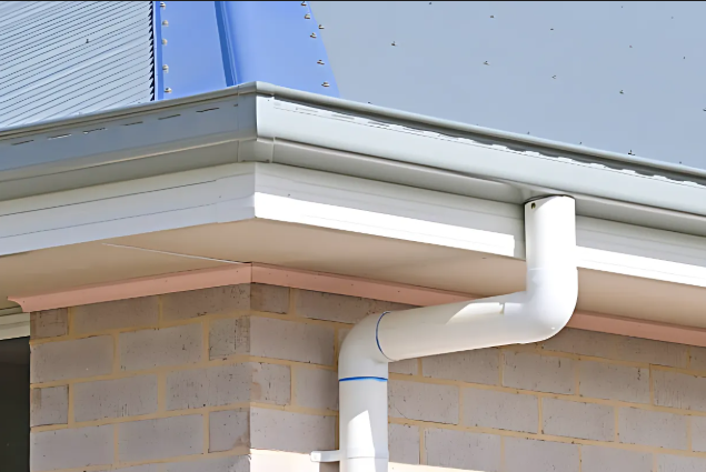 Gray gutters and downspout on a building with a white soffit and a brick exterior.