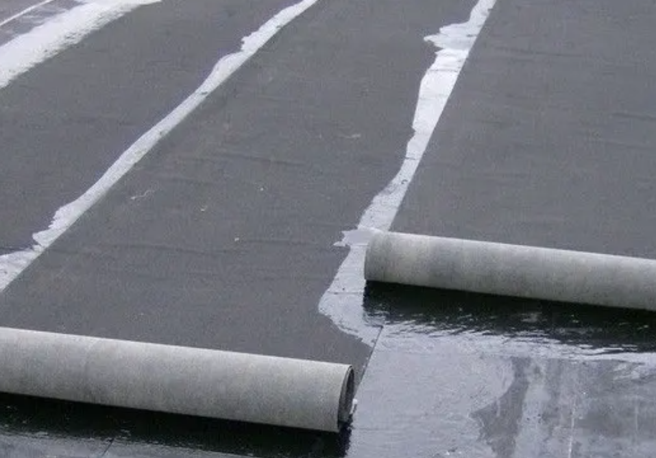 Rolls of roofing material being applied to a flat roof, with wet sealant visible.