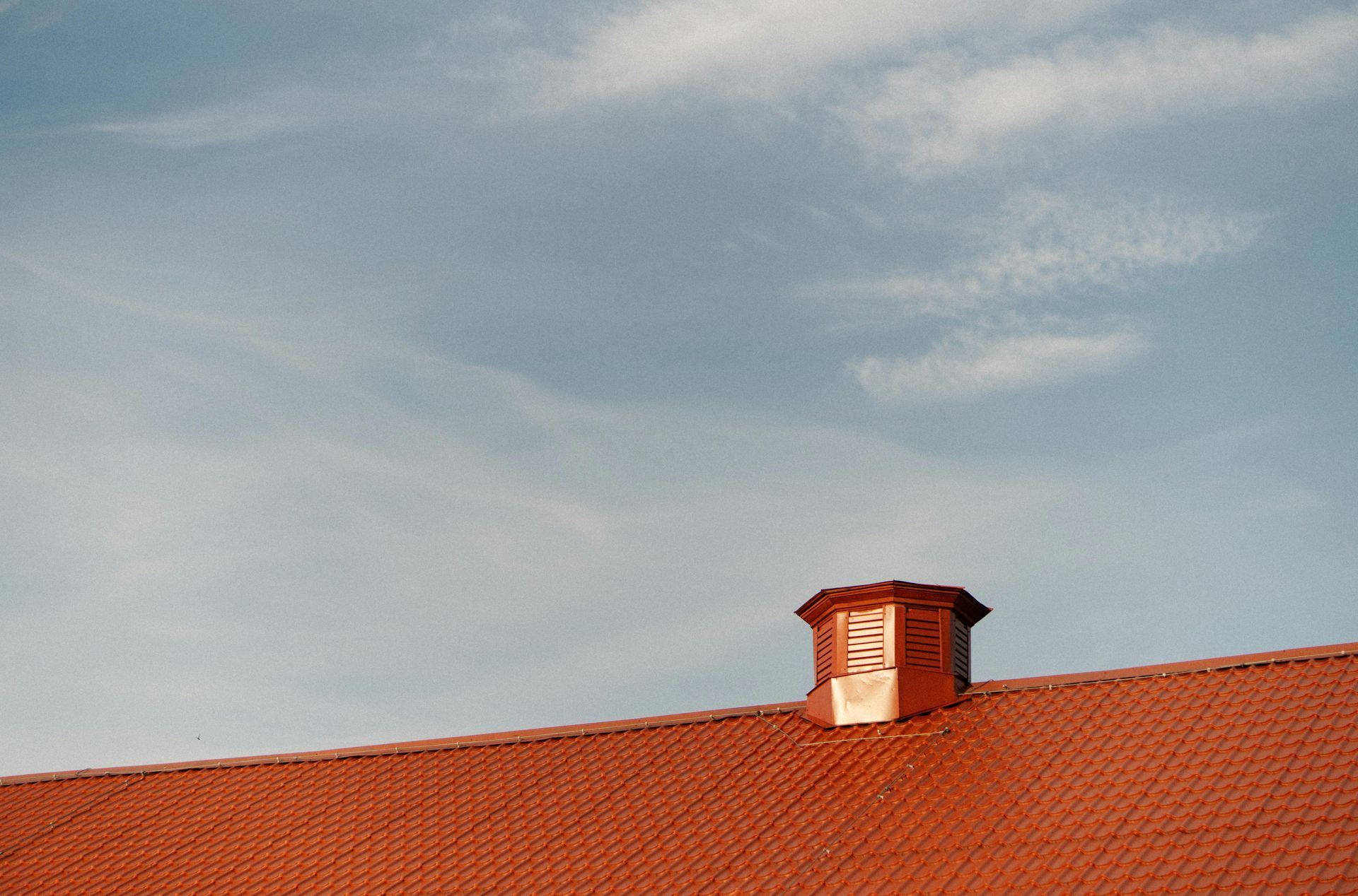 Red tiled roof with copper vent against a blue sky.