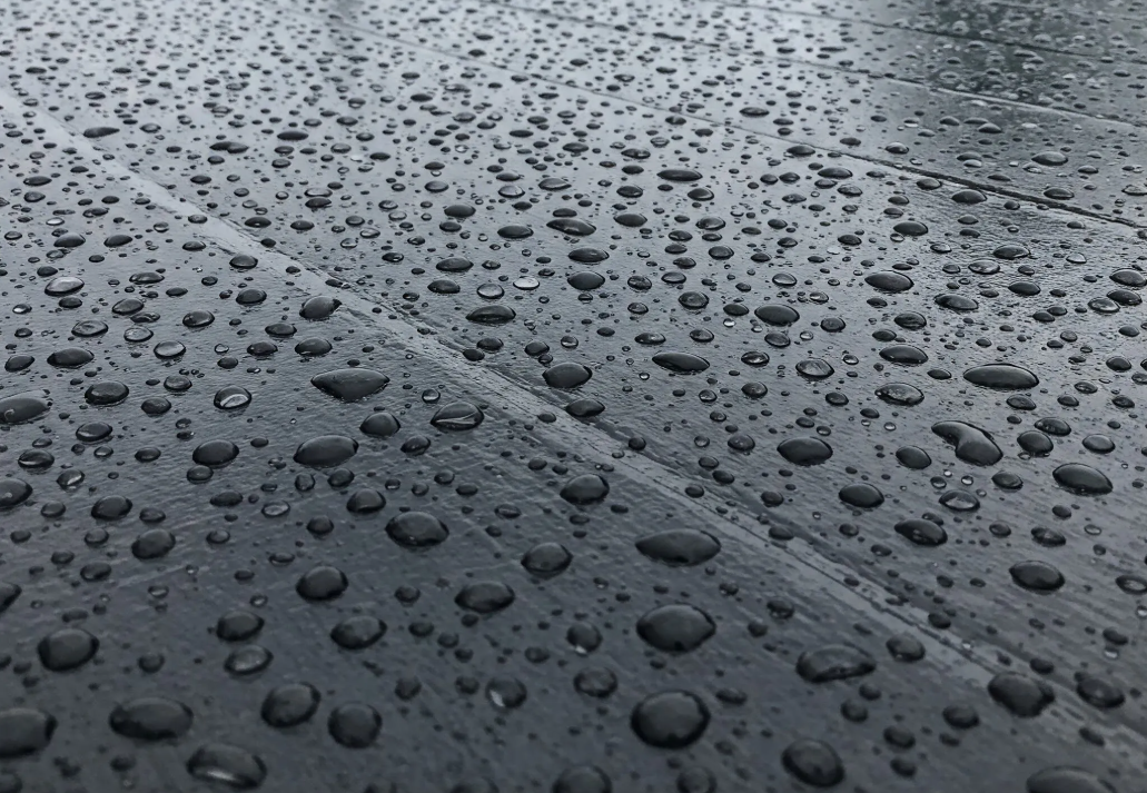 Raindrops on a dark, reflective surface, creating a textured pattern.