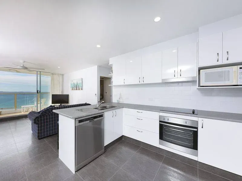 Modern white kitchen with ocean view. Features stainless steel appliances and gray countertops.