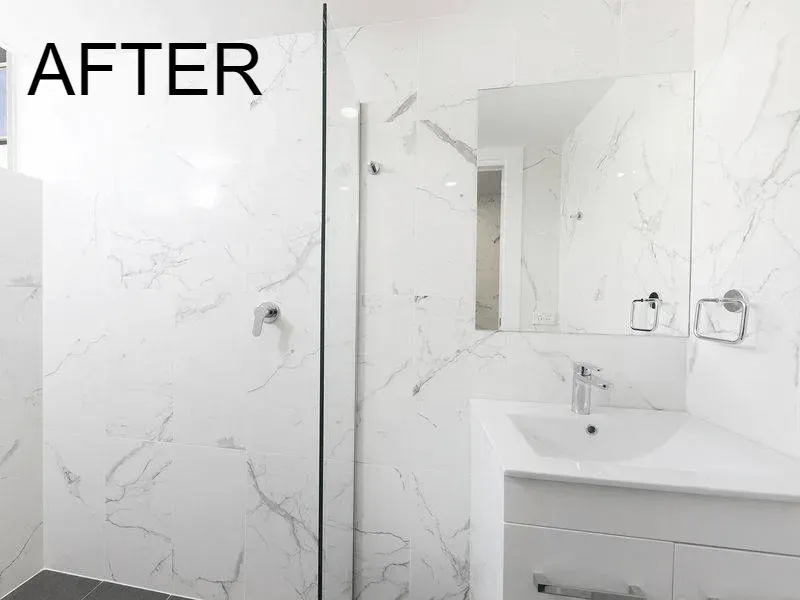 White marble-tiled bathroom with a glass shower, a white vanity, and a mirror; 