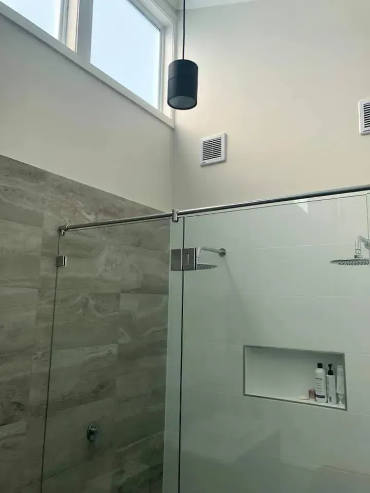 Bathroom with glass shower, tiled walls, overhead light, and a small window.