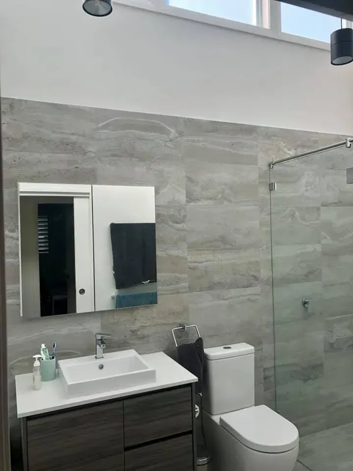 Modern bathroom with gray tile, a white toilet, sink, and glass shower.