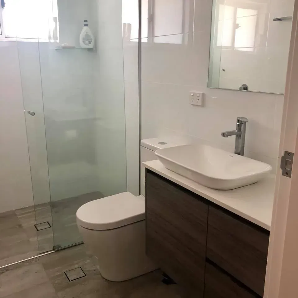 Modern bathroom with shower, toilet, vanity, and window. Gray tile floor, white walls, and wood vanity.