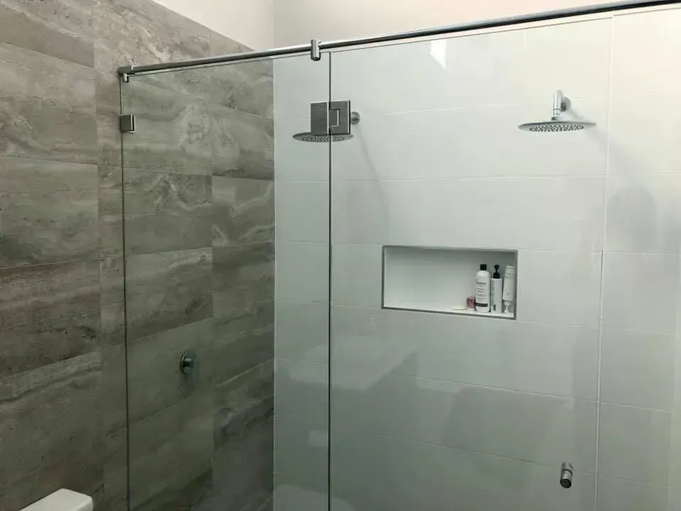 Glass-enclosed shower with two showerheads, built-in shelf, and gray tile.