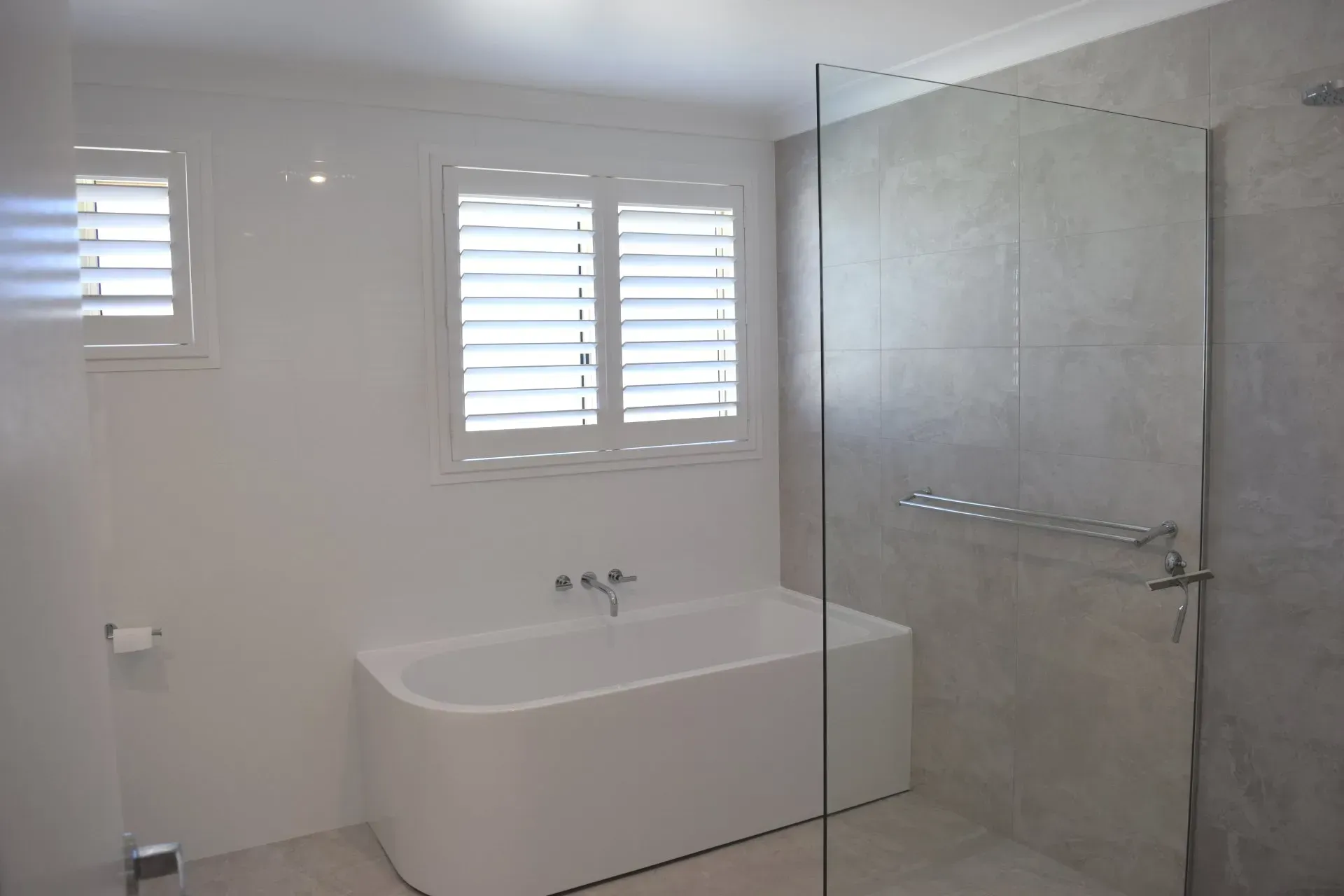 White bathroom with a modern bathtub, shower, and window shutters.