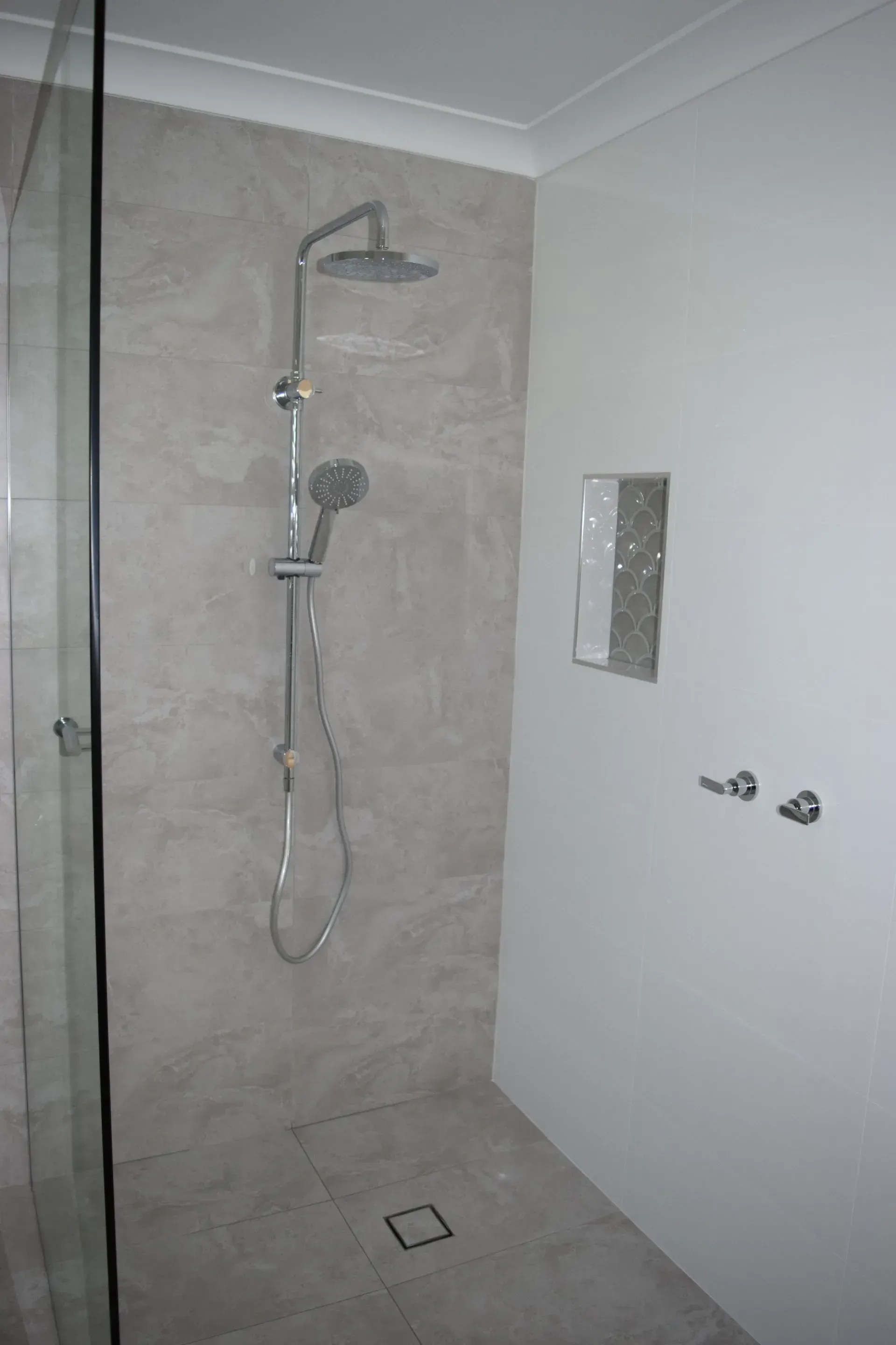 Shower stall with gray tiled walls and floor, a glass door, and silver fixtures.