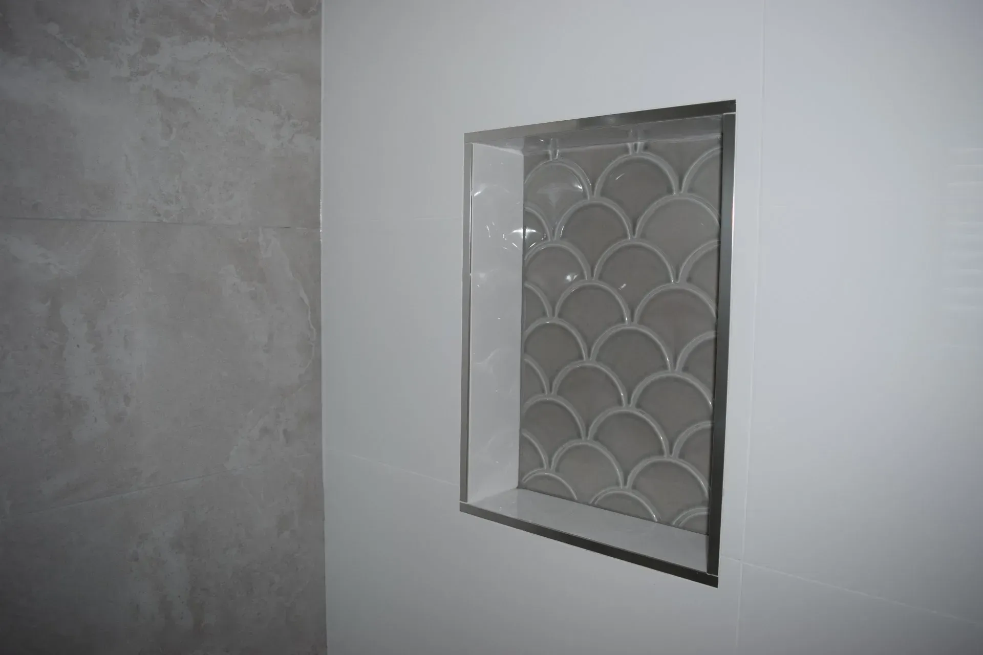 Recessed shower niche with grey fan-shaped tile in a white wall.