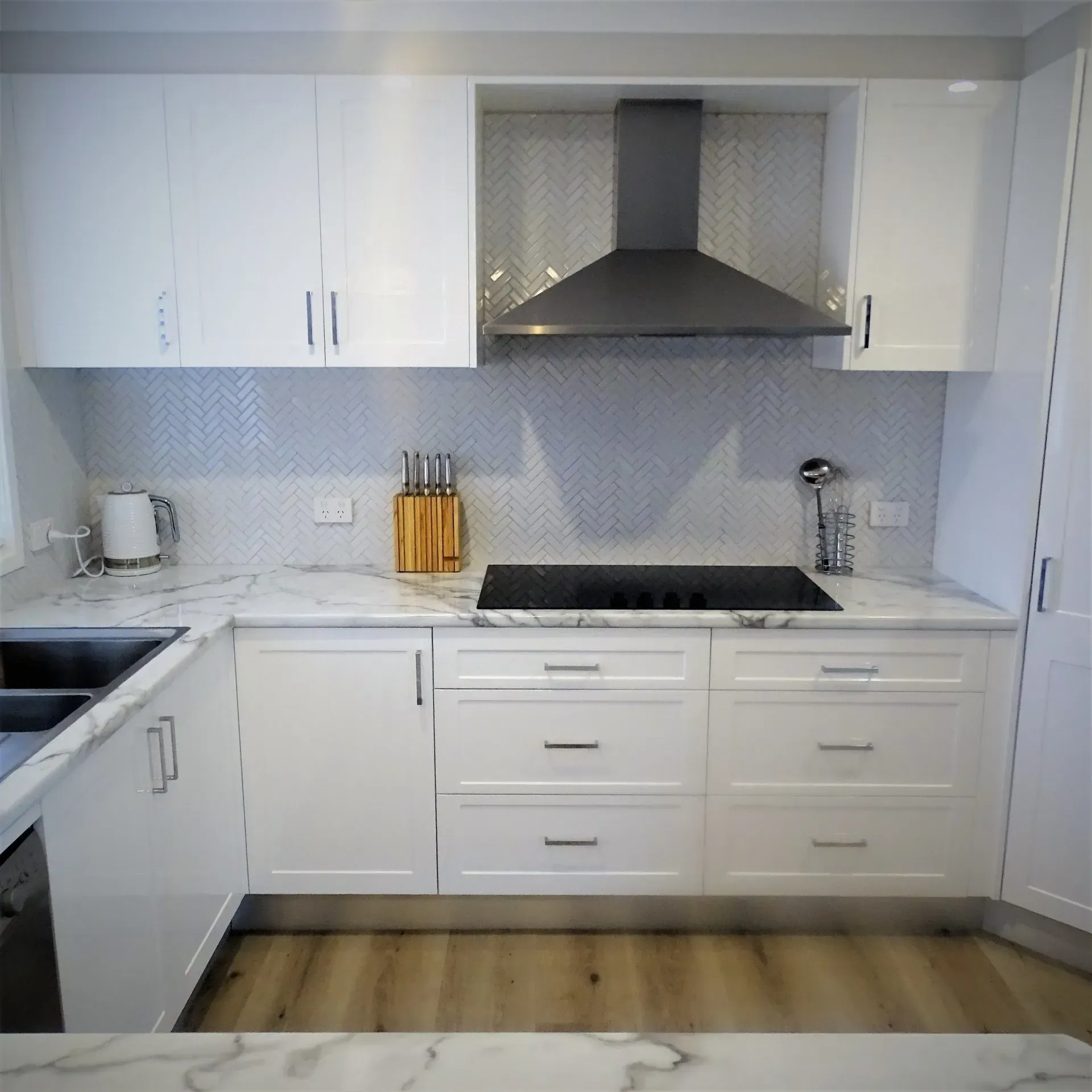 White kitchen with marble countertops, white cabinets, and stainless steel range hood.
